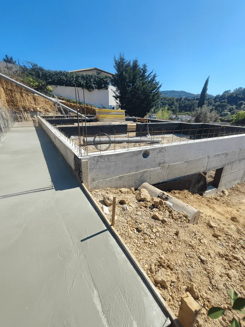 Surface en béton fraîchement réalisée le long de soubassements en construction.