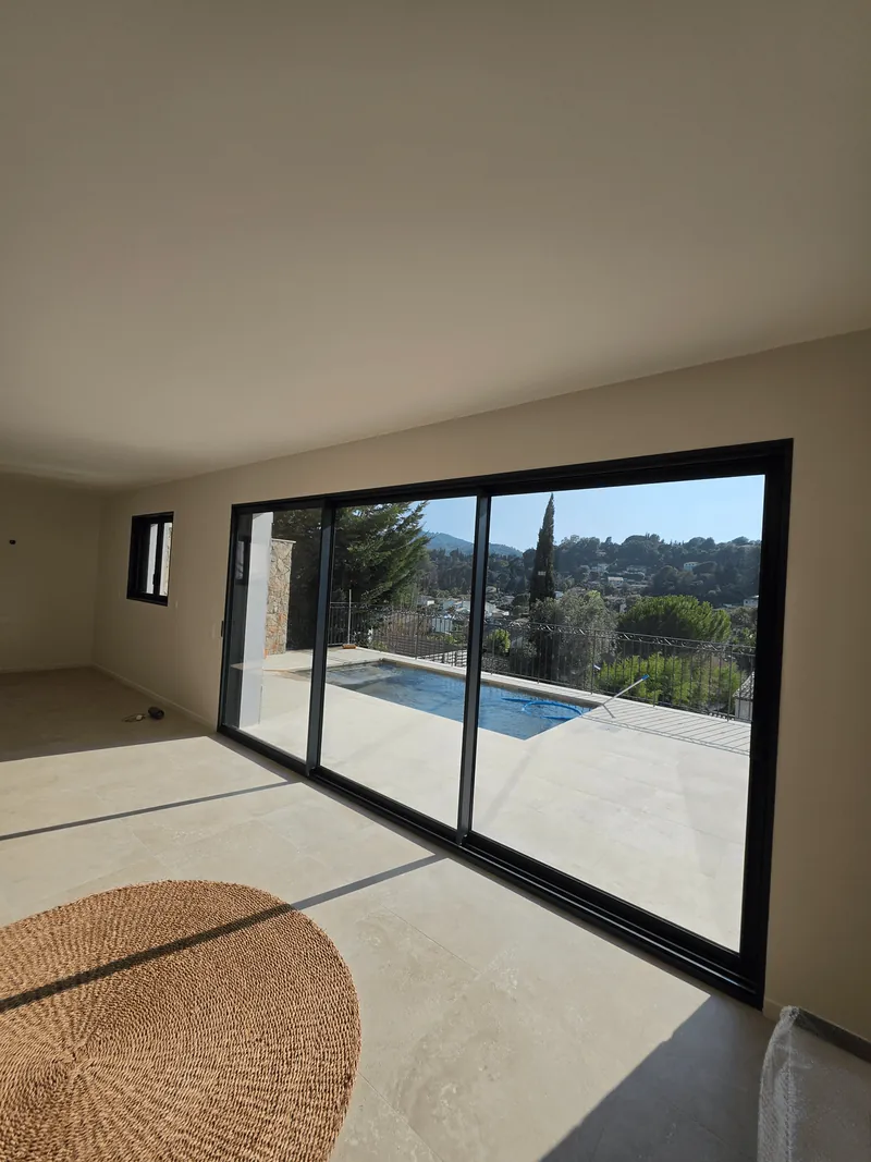 Pièce rénovée avec un sol clair et une grande baie vitrée donnant sur une terrasse.