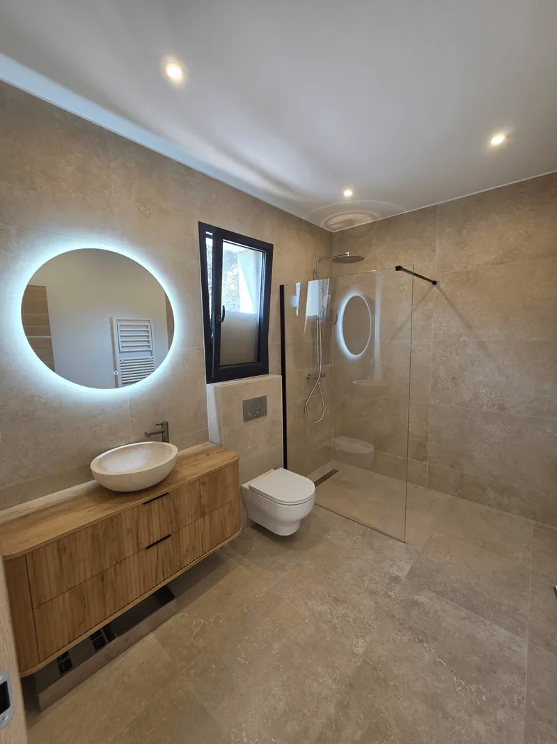 Salle de bain avec une vasque, un miroir rond éclairé et une douche vitrée.